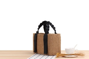 Close-up of a woven paper rope tote bag featuring black ruffled ribbon handles on a wooden table