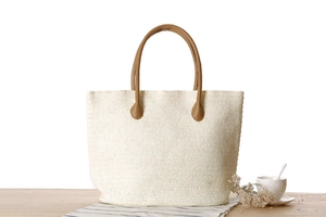 Detail of woven straw tote bag with brown faux leather straps on a wooden table