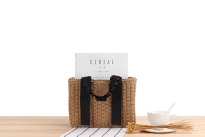 Detailed close-up of woven paper straw tote bag featuring ruffled black ribbon handles