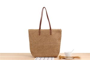 Detailed texture of handwoven straw tote bag with brown leather handles on wooden table
