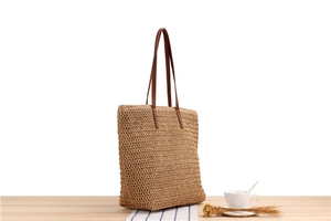 Detail view of woven straw tote bag texture and brown leather strap on wooden surface