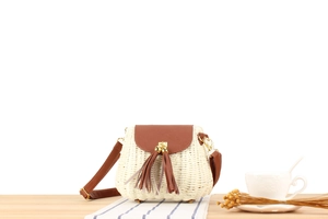 Détail d'un sac en papier tissé main avec rabat en cuir marron et glands sur une table