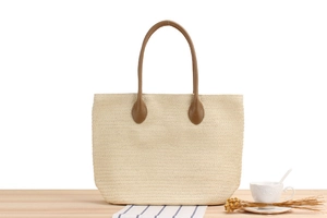 Close-up of woven straw tote bag with brown leather handles on a cafe table setting