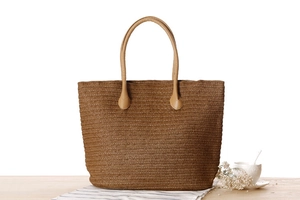 Detail of coffee-colored paper rope woven tote bag with brown handles on wooden table