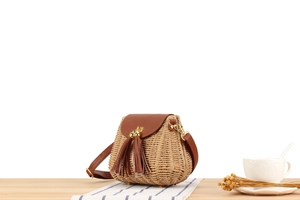Détail d'un sac bandoulière en paille tressée avec rabat en cuir et glands sur la table