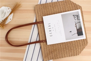 Detail of hand-woven straw tote bag with brown faux leather handles on wooden surface