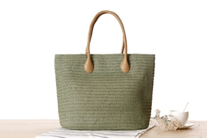 Close-up of woven straw tote bag in sage green with brown faux leather handles