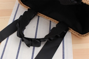 Detail of woven straw bag showing black ruffled grosgrain handle and inner cotton lining