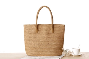 Detail of hand-woven straw tote bag with round brown faux leather handles for summer travel