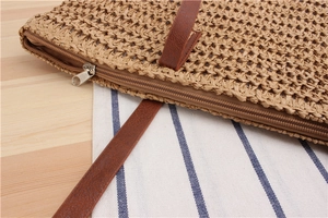 Close-up of the metal zipper and brown faux leather handle on a straw woven shoulder bag