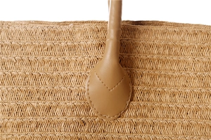 Macro detail of the brown leather handle attachment on a woven paper straw shoulder bag