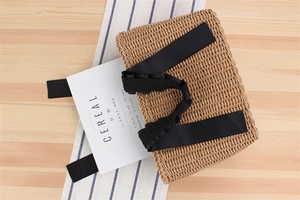Close-up of woven straw tote bag featuring black ribbon handles on a wooden table