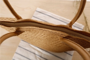 Detailed close-up of zipper closure and leather handle on a woven paper straw shoulder bag