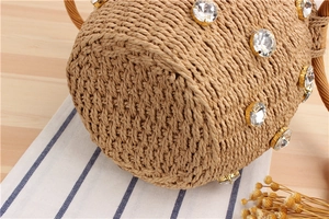 Close-up of khaki woven bucket bag with large rhinestones on a warm wooden surface
