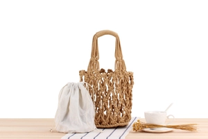 Detail of khaki macrame woven tote bag with white cotton drawstring lining on a wooden table