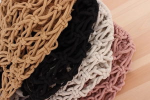 Detailed view of woven mesh bags in various colors on a light wood background