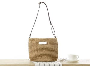 Detail of paper rope woven crossbody bag with brown straps on a minimal wooden table