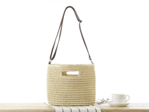 Detail of handwoven paper straw bag featuring cutout handle and brown leather strap