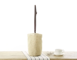 Detail of paper straw woven bucket bag with brown leather strap on wooden surface