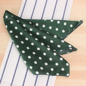 Détail d'un foulard en soie vert foncé à pois blancs sur une surface en bois