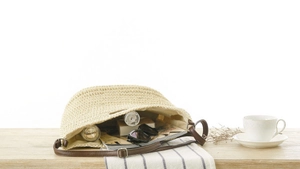 Detail shot of woven paper straw bag with brown leather strap and silver buckle adjustment