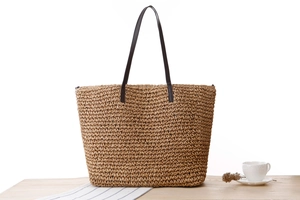 Détail d'un sac cabas en corde de papier tressé avec anses marron sur table boisée