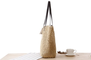 Détail du sac bandoulière en paille de papier avec poignées en cuir sur une table