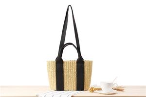 Detail of woven straw tote bag with black canvas straps on a casual wooden table setting