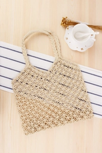 Detail of hand-woven hollow mesh tote bag in beige on a rustic wooden table setup