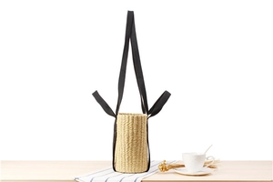 Detailed view of cylindrical straw bag with black canvas straps and tight woven texture