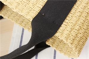 Macro detail of beige woven straw tote bag with reinforced black canvas handles