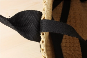 Detail of hand-woven straw tote bag with black canvas handle stitching on wood background