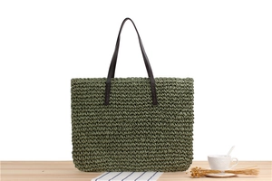 Detail of dark green woven paper rope tote bag with brown handles on wooden surface