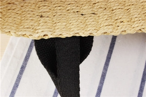 Close-up of tight spiral weave texture and reinforced black strap on straw bag