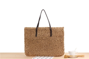 Close-up of woven paper rope texture with dark brown leather handles on a summer shoulder bag