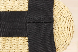 Close-up of natural straw weaving with cross-stitched black canvas straps and fine texture
