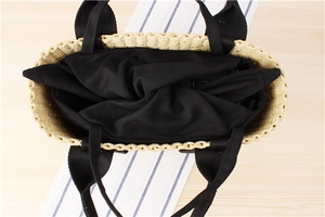 Internal detail of a woven straw tote bag featuring black canvas lining and zipper closure