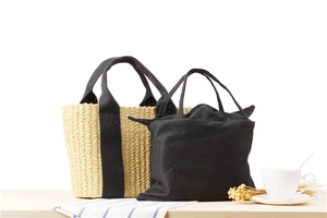 Detail of woven straw tote bag and black canvas insert bag on a bright wooden surface