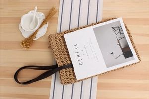 Detail of woven straw tote bag with brown handles on a wooden table for daily use