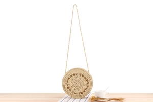 Detail of round straw bag with hollow floral weave and slim woven strap on wooden table