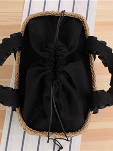 Handwoven straw tote bag with black ruffle handles and drawstring liner on a wooden desk