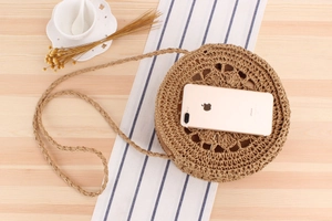 Close-up of circular straw woven shoulder bag with intricate cutout floral patterns