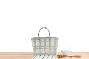Detail of light green and white plaid woven basket on a light wood tabletop with flowers