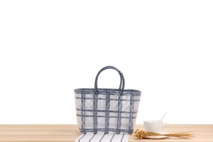 Detail of blue and white plaid woven tote bag on a wooden table with coffee and flowers