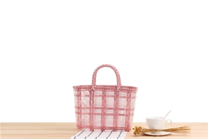 Detailed view of pink checkered woven beach bag on a light wood tabletop with flowers
