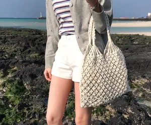 Close-up of beige woven tote bag with thick handles against a scenic beach backdrop
