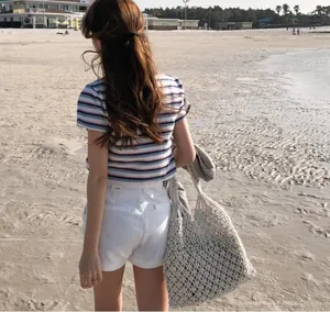 Outdoor shot of a beige woven tote bag paired with a striped T-shirt and white shorts