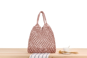 Detail of hand-woven hollow pattern shoulder bag in dusty rose cotton rope on wood table