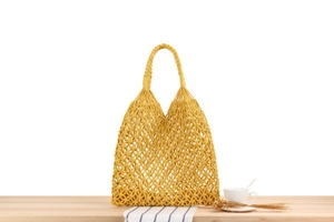 Detail of yellow macrame woven tote bag with intricate geometric patterns on wooden table