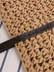 Minimalist straw woven tote bag with brown leather strap detail on striped background